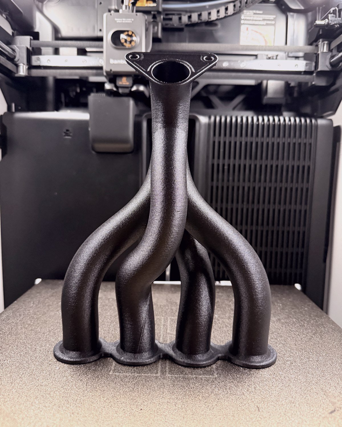 An exhaust manifold printed in black filament on the machine