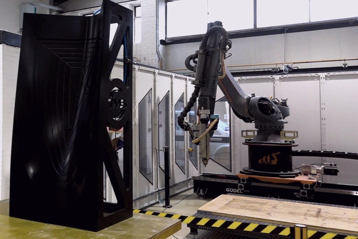 A tall printed tool beside a robotic extrusion arm